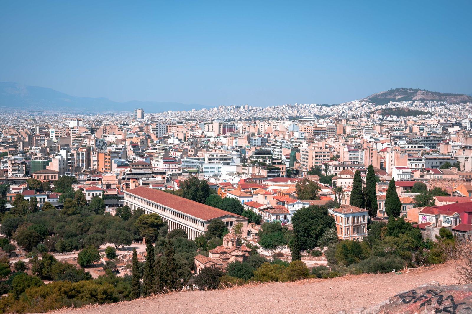 Athens rooftops and the Stoa of Attalos seen from a hillside, with Lycabettus in the distance